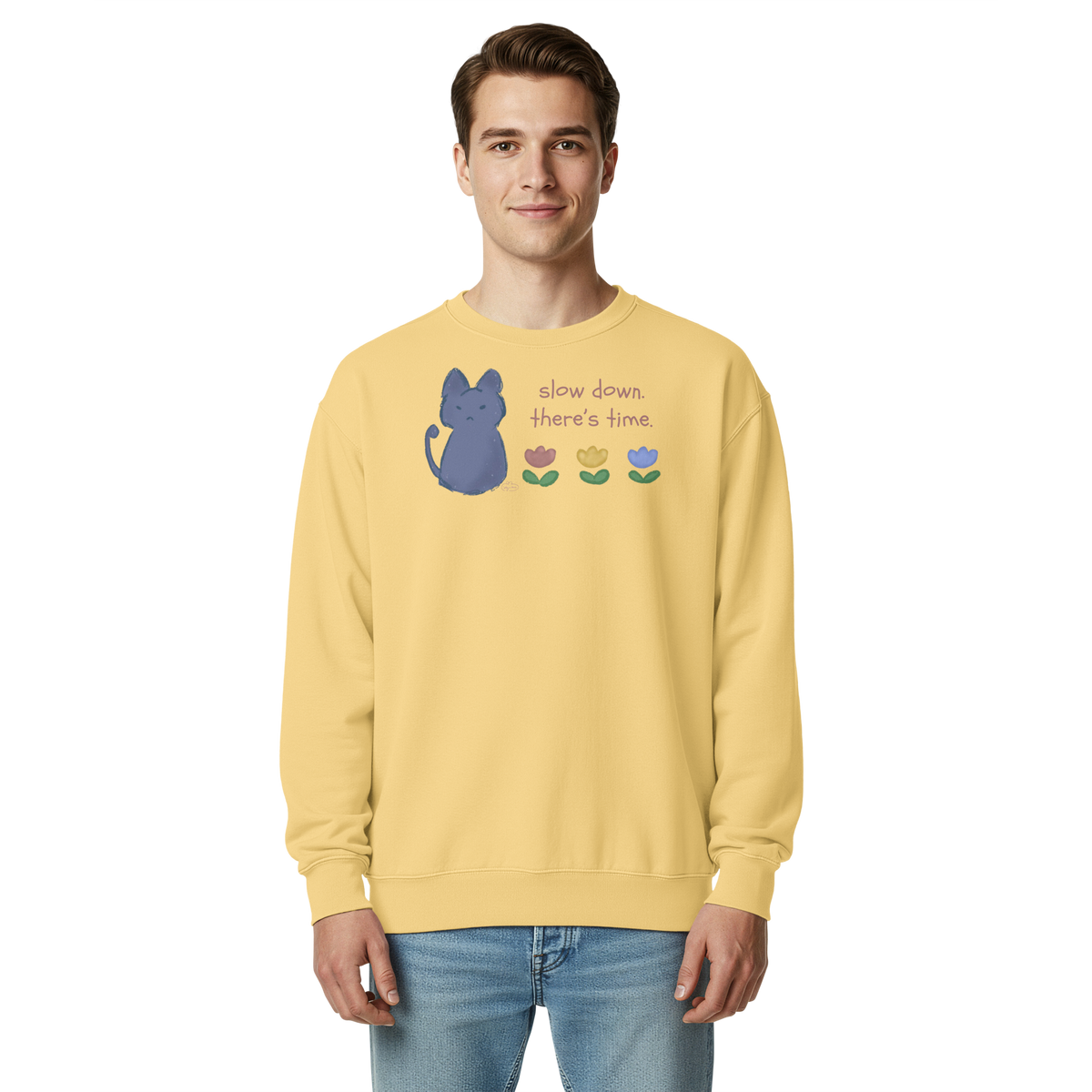 Model wearing a butter yellow garment-dyed sweatshirt with a blue cat, three flowers, and 'Slow down, there's time' lettering.