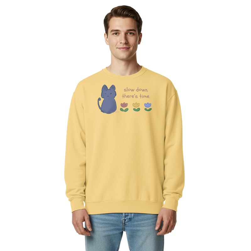 Model wearing a butter yellow garment-dyed sweatshirt with a blue cat, three flowers, and 'Slow down, there's time' lettering.