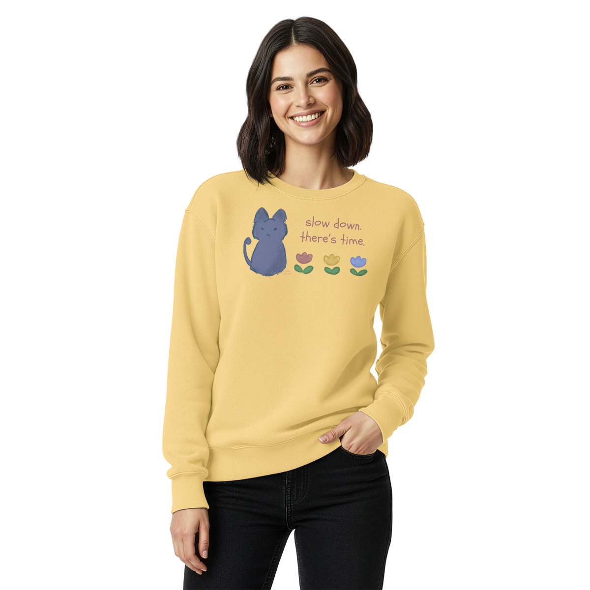 Model wearing a butter yellow garment-dyed sweatshirt with a blue cat, three flowers, and 'Slow down, there's time' lettering.