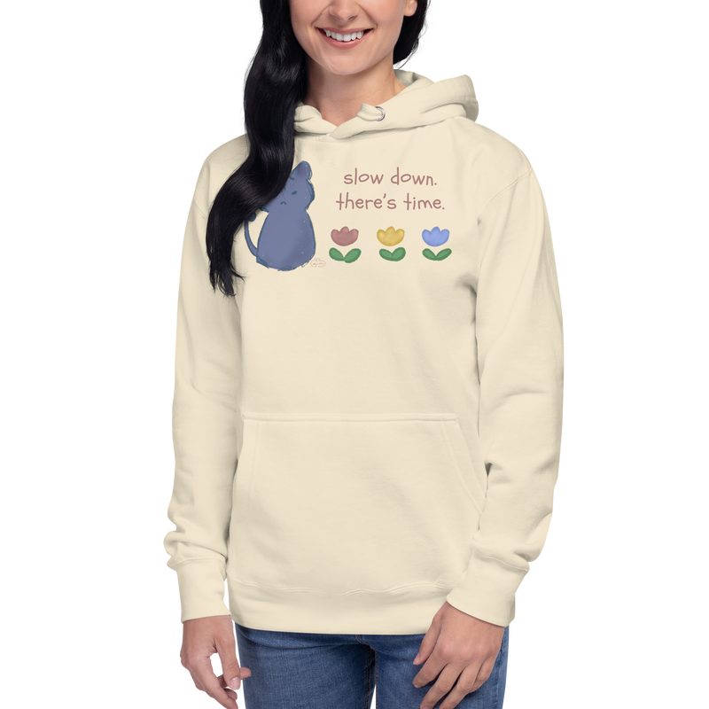Model wearing a bone cream pullover hoodie with a blue cat, three flowers, and 'Slow down, there's time' lettering.
