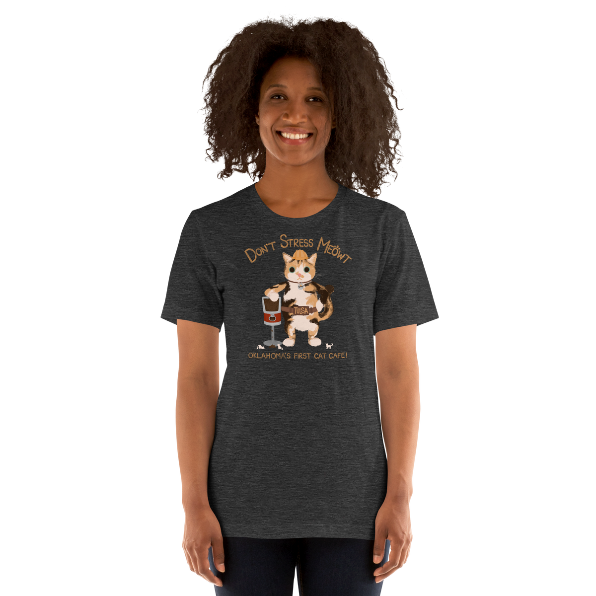 Model wearing a dark heather grey Bella + Canvas T-shirt with a calico cowboy cat and Don't Stress Meowt cat cafe lettering.