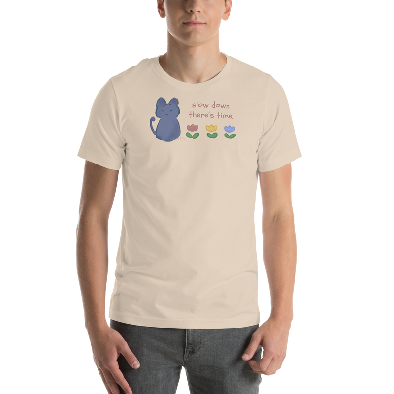 Model wearing a soft cream Bella + Canvas T-shirt with a blue cat, three flowers, and 'Slow down, there's time' lettering.