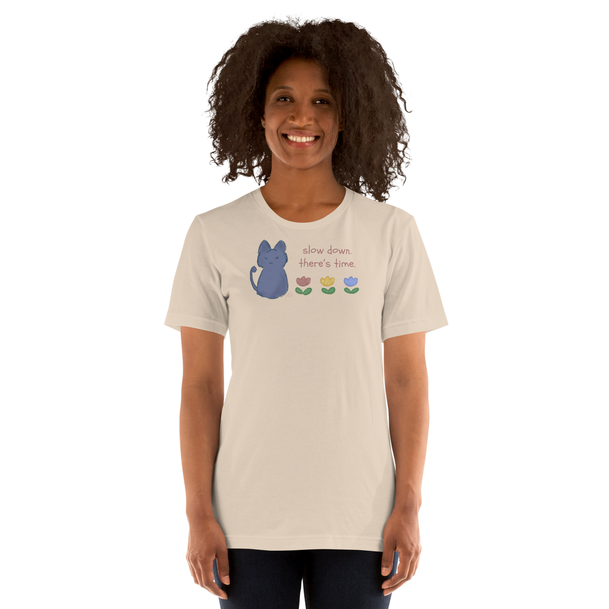 Model wearing a soft cream Bella + Canvas T-shirt with a blue cat, three flowers, and 'Slow down, there's time' lettering.
